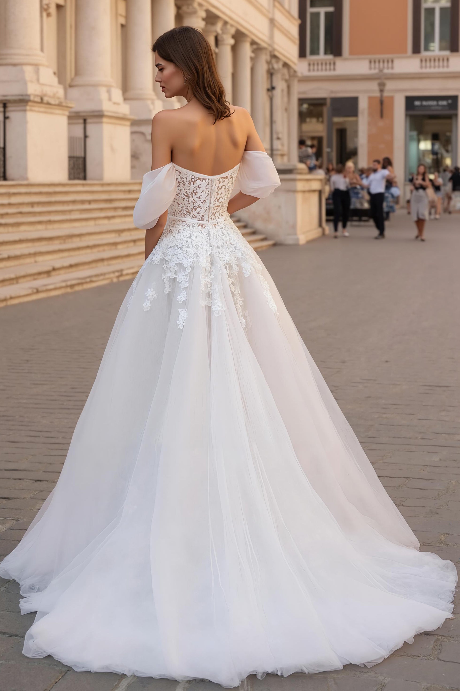 Robe de mariée ivoire avec des appliques, décolleté épaules dénudées, coupe trapèze et traîne.