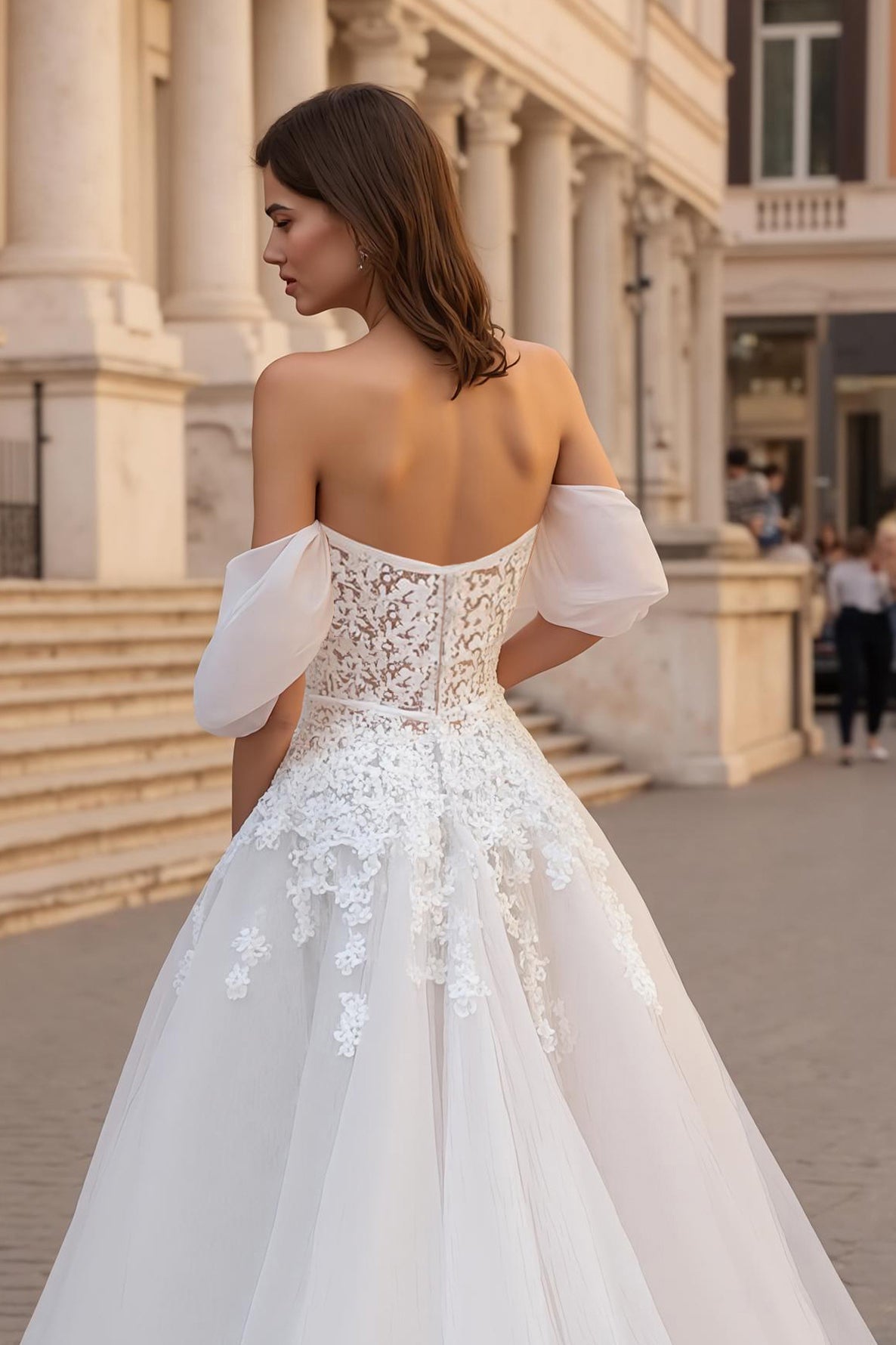 Robe de mariée ivoire avec des appliques, décolleté épaules dénudées, coupe trapèze et traîne.